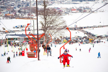 Little girl in red winter overall using chairlift in Bakuriani ski resort, Georgia