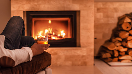 Man sitting at home by the fireplace and drinking a whiskey.  