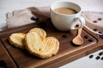 Cup of coffee with snacks on wooden cutting board on white wooden table