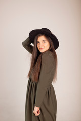 Fototapeta premium Young sensual caucasian woman in dark green (olive) dress holding fedora hat isolated on white-grey background with beautifull smile