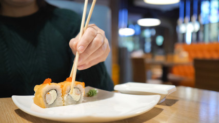 The concept of Japanese and Chinese cuisine. The unknown girl in the restaurant has wooden chopsticks sushi and rolls.