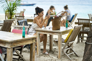 Tanned woman using her smartphone in outdoor restaurant on tropical beach