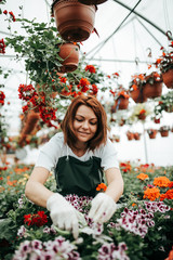 Redhead young woman working in greenhouse and enjoying in beautiful flowers. Female worker working...