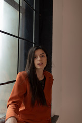 Fototapeta premium portrait of an attractive sexy girl dressed in a stylish suit sitting on the window sill near a large window
