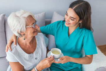Young caregiver in uniform hugging smiling elderly woman during a home visit