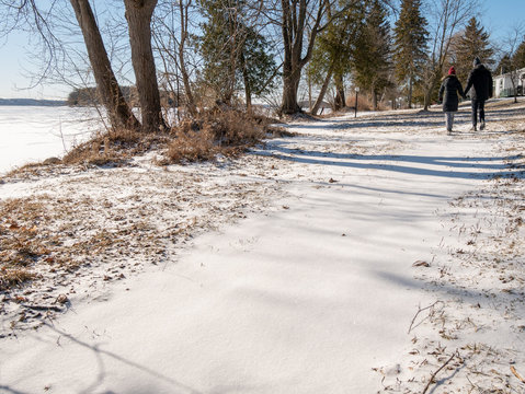 Couple walking along snowy path near a lake in winter