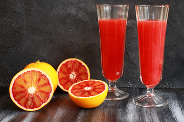 Orange juice with cut blood oranges on dark board