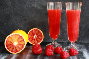 Orange juice, blood orange and raspberries on dark board