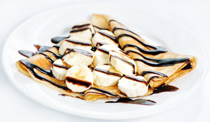 Thin delicious pancake with banana and chocolate on white .