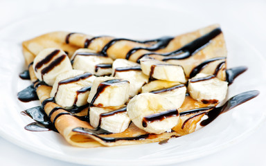 Thin delicious pancake with banana and chocolate on white .
