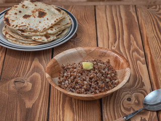 Buckwheat porridge in a deep plate and a stack of freshly baked tortillas on a wooden table