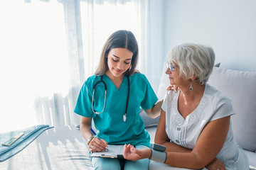 Nurse doing blood pressure monitoring for senior woman at home