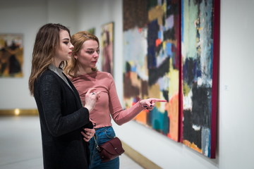 two girls discuss paintings in Gallery of modern art - obrazy, fototapety, plakaty