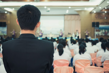 Speaker presentation talk on stage in lecture hall at school or university workshop. Rear view smart businessman or teacher male audience listening in conference. Business meeting and seminar concept