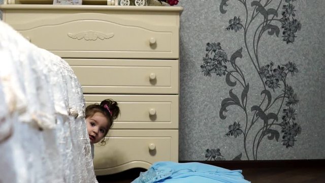 Little girl hiding and peeking out from behind the bed