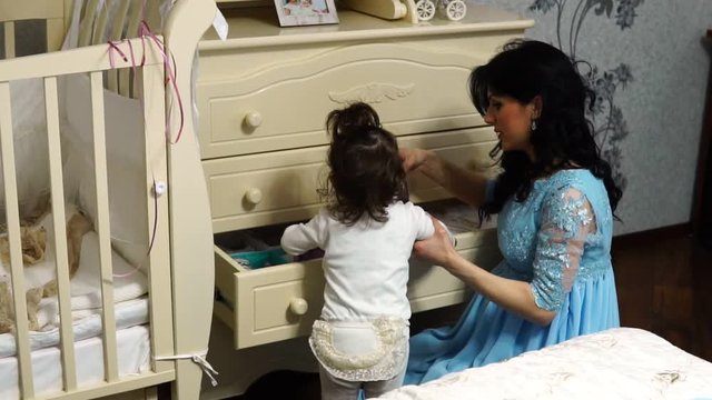 Young mom Little baby girl pulls out of the dresser clothes