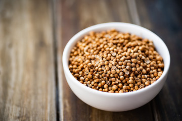 Dried coriander seeds in a bowl on wooden table, herbs and spices, food ingredient