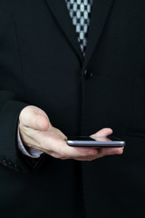 Businessman in Black Suit and Tie Holding Smartphone in Hand Against White Background