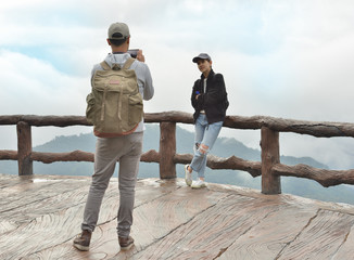 Tourist man using smartphone taking picture of her girlfriend on mountain landscape (Thailand)