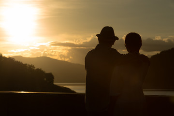 Image of sunset on orange and yellow horizon with a silhouette of a senior couple in natural surrounding