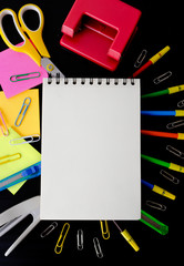 Bright multicolor school stationary supplies on black background.  Colored pencils ruler notepad sticky notes cutter paper clip scissor paper puncher top view with copy space