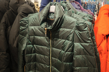 Rack with trendy warm coats of green color in clothes shop, close up