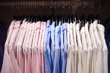 Elegant light blouses hanging on metal rack in modern clothes shop