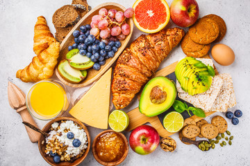 Healthy balanced breakfast on white background. Muesli, juice, croissants, cheese, biscuits and fruit, top view.