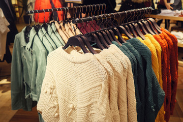 Rack with hangers of various colorful sweaters for sale in modern clothes store, toned