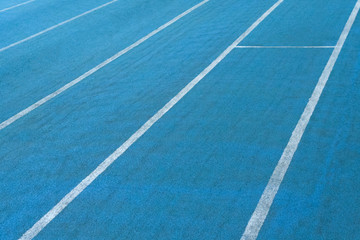 Fragment of blue synthetic surface of running tracks  of athletics stadium with white lines as texture, background (abstract)