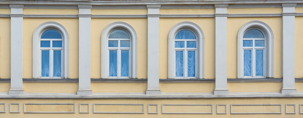 Close up view on a facade of ancient yellow building with four arched windows and white pilasters...