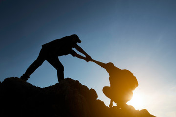 Asia couple hiking help each other silhouette in mountains with sunlight.Silhouette man lifts his hand on a rocky seashore. 