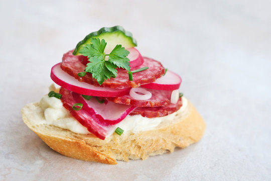 Single piece of tasty appetizer, slice of brad with slami, cheese, red radish cucumbers and spring scallions on a marble tile.