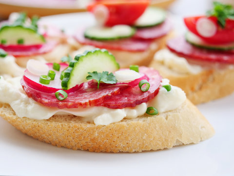 Tasty appetizer, slices of brad with slami, cheese, red radish cucumbers and spring scallions on a marble tile.