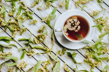 White cup and dish of linden tea on linden blossom background. Herbal medicine concept. Rustic. Top view.