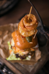 A huge stacked double cheeseburger, with bacon, cheese, lettuce, topped with gherkins, onion rings and cherry tomato. photographed in a rustic mechanic workshop background.