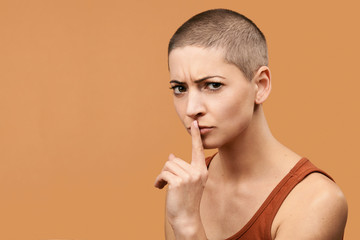 Attractive mid 30s woman pressing finger to lips as if asking to keep silent. Photo of young angry woman making Shhh gesture.