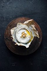 A beautiful organic round slab of baked brie cheese with garlic slices on the top. Photographed in a dark moody atmospheric gritty modern contemporary setting. Rusty plate