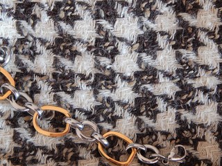 Trendy tweed houndstooth fabric in elegant combination with golden chain. 80`s style concept.