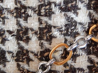 Trendy tweed houndstooth fabric in elegant combination with golden chain. 80`s style concept.