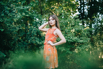 Fototapeta premium Beautiful young girl in a summer red dress in a park