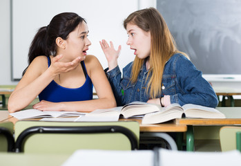 Two girl are sitting at the desk and talking about life