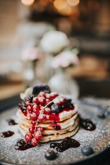 Traditional homemade dish for Pancake Day, shrove Tuesday. Stack of pancakes with blueberries, cranberries, blackberries and jam, covered in icing sugar. 