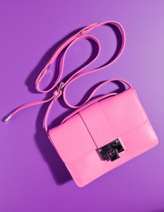 A beautiful expensive womans pink leather handbag against a complimentary purple coloured...
