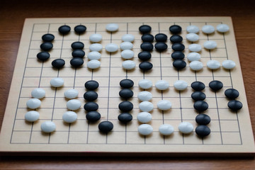 Inscription game over, made on the board for the game of Go by stones for the game of Go.  This is a metaphor for AI's victory in the game of Go over man. Flat lay style