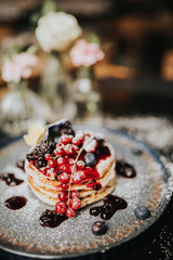 Traditional homemade dish for Pancake Day, shrove Tuesday. Stack of pancakes with blueberries, cranberries, blackberries and jam, covered in icing sugar. 