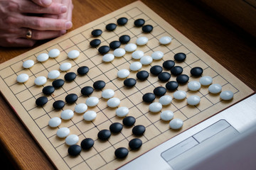  men's hands on a laptop and between them a Go game board with the inscription "Game over". It is a symbol of the victory of AI over a person in the game of Go.