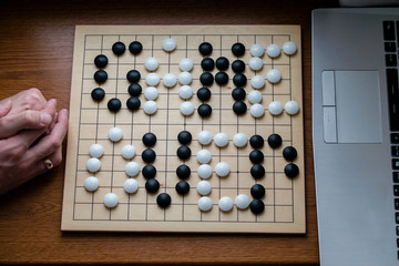 men's hands on a laptop and between them a Go game board with the inscription "Game over". It is a symbol of the victory of AI over a person in the game of Go. Flat lay style