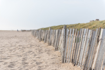 Fototapeta na wymiar Beautiful seaside weathered wooden fences on a beautiful relaxing calm sandy beach with sand dunes behind, shot with a shallow depth of field. Nature reserve.