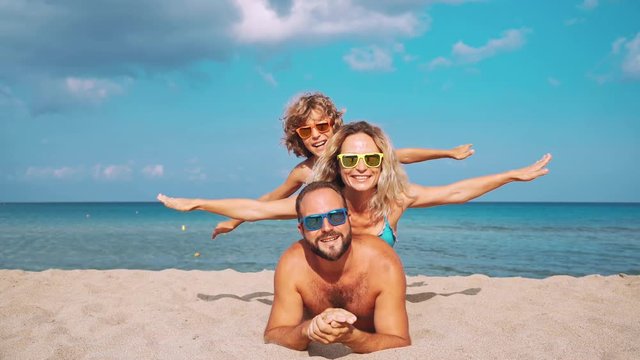 Happy family lying on the beach. People having fun on summer vacation. Father, mother and child against blue sea and sky background. Holiday travel concept